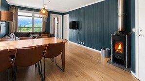 A modern living room with a wooden dining table, leather chairs, a fireplace, a TV mounted on the wall, and a view of the outdoors. - Ski in/Ski out with Sauna and Modern Mountain Comfort (Hemsedal)