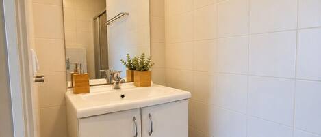 A bathroom with a white vanity, a mirror, a towel rack, and a potted plant.