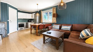 A modern living room with a brown leather sofa, wooden coffee table, and a dining area with a wooden table and chairs. - Ski in/Ski out with Sauna and Modern Mountain Comfort (Hemsedal)