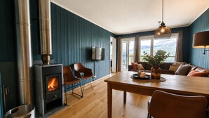 A modern living room with a wood-burning stove, a dining area with a table and chairs, a sofa set, and a television mounted on the wall. - Ski in/Ski out and Perfect for Families (Hemsedal)