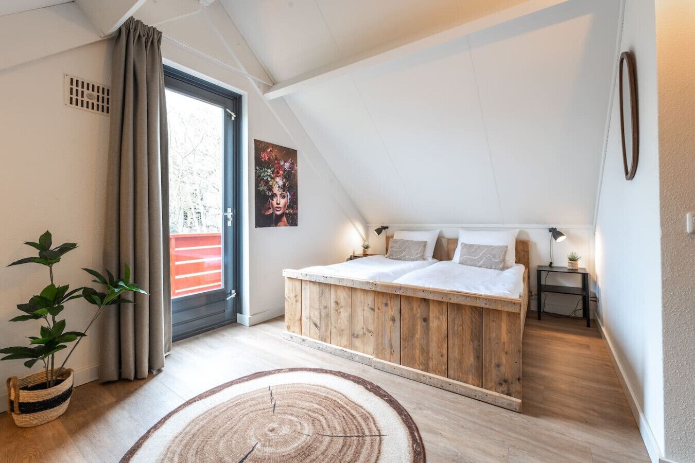 Un dormitorio con techo inclinado, una cama con ropa de cama blanca, una mesita de noche con lámpara y una planta en maceta.