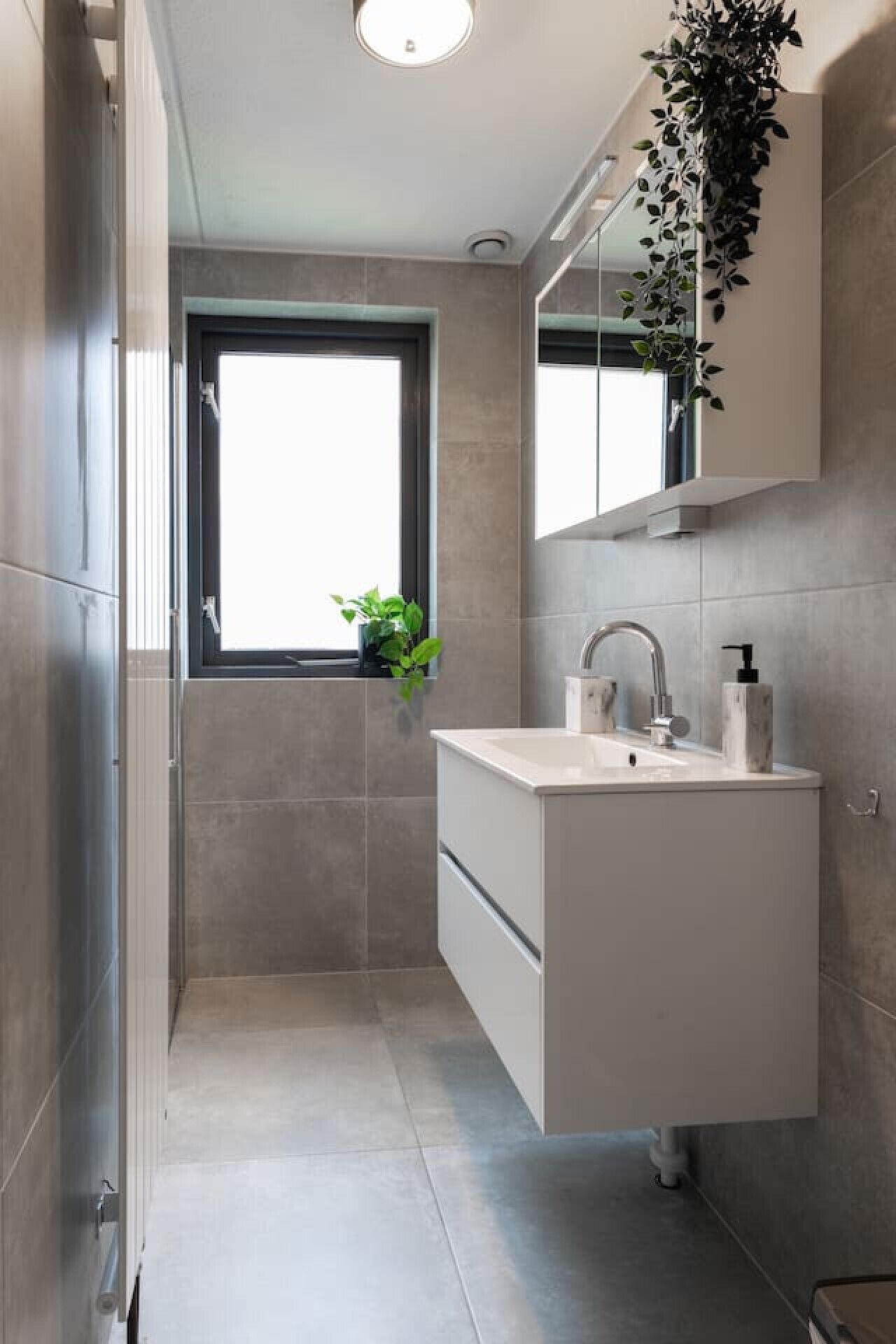 A modern bathroom with a large window, a sink with a mirror, and a potted plant.