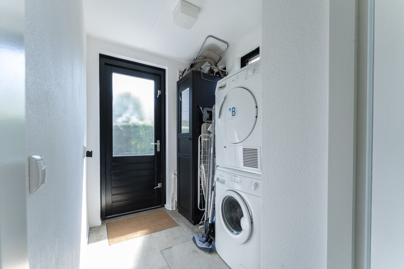 A laundry room with a washing machine and dryer, a door leading outside, and a small window.