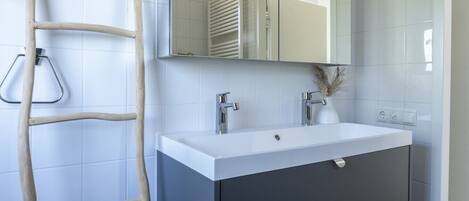 Un baño con un lavamanos blanco, muebles oscuros, un espejo y una escalera de madera.