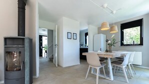 Une cuisine moderne avec un îlot central, des chaises blanches, une table à manger, une cuisinière noire et des luminaires suspendus.