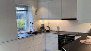 Une cuisine moderne avec des meubles blancs, un plan de travail noir et une fenêtre donnant sur un paysage verdoyant.