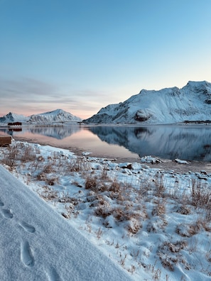 A snowy landscape with a calm lake, mountains, and a wooden dock.