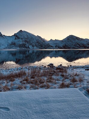 A snow-covered landscape with a calm lake and mountains in the background.