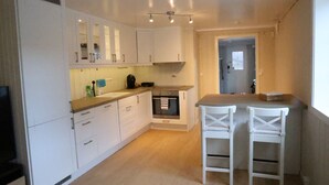 A compact kitchen with white cabinets, a built-in oven, and a small bar area with two white stools. - Central apartment in Lillehammer (Lillehammer)
