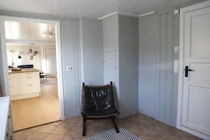 Ein Zimmer mit einem Sessel, einer Tür und Blick in einen anderen Raum mit Küchenzeile.