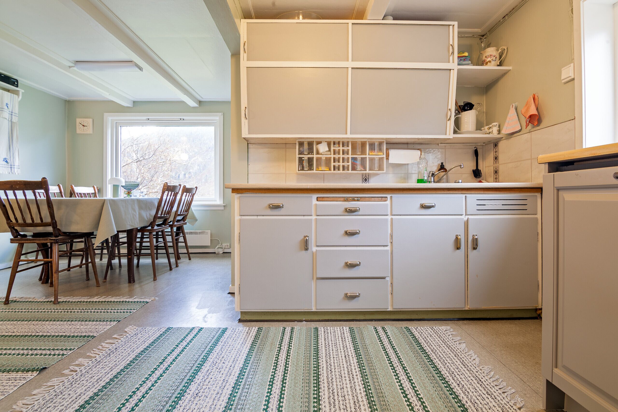 Une cuisine avec des meubles blancs, une table à manger avec des chaises et une fenêtre.