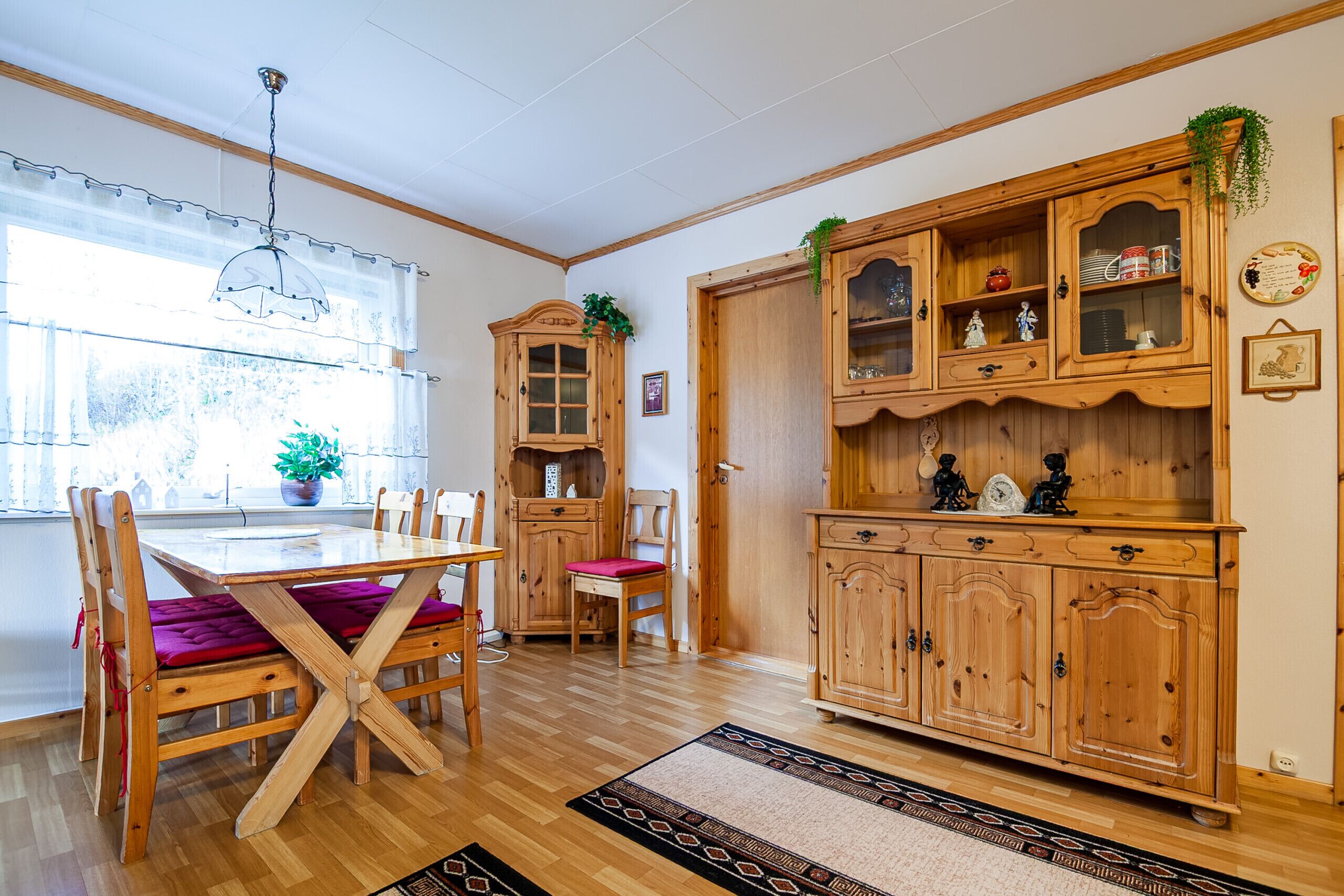 A dining area with wooden furniture, a window with curtains, and a cabinet with glass doors.