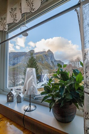 A window with a view of mountains, a potted plant, and a lamp on a windowsill. - Valen Retro Home, Reine (Moskenes)