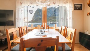 A dining area with a wooden table and chairs, a chandelier, and a view of mountains through a window.