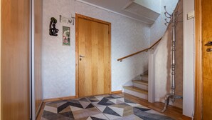 A hallway with a geometric-patterned rug, a wooden door, a staircase, and a metal coat rack.