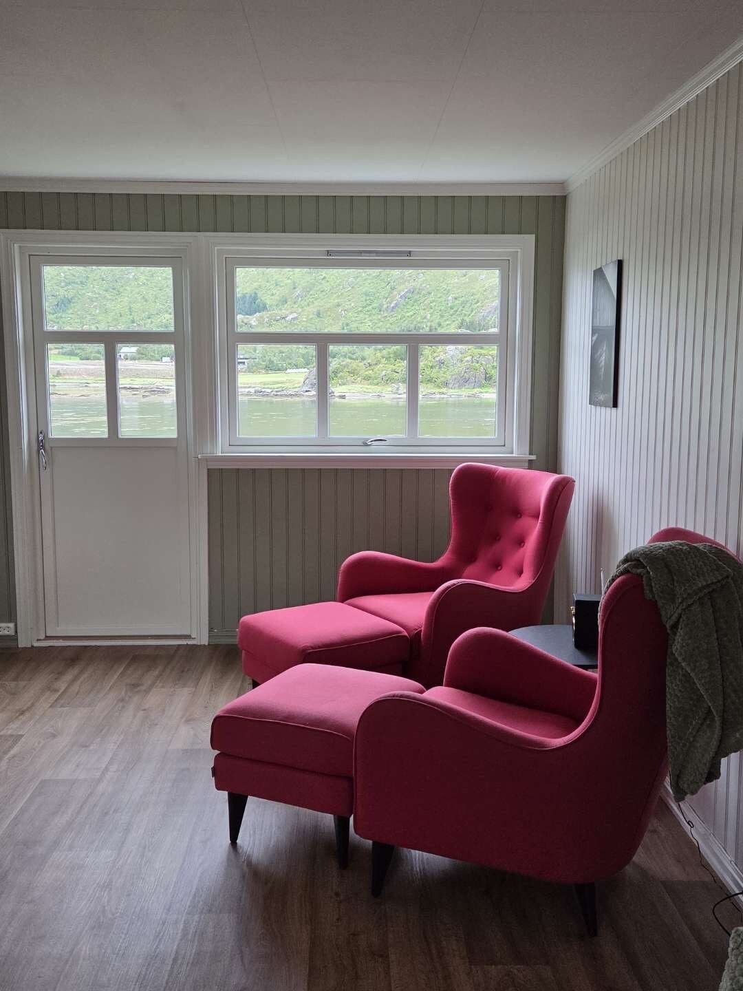 Une pièce dotée d’une grande fenêtre, d’un fauteuil recouvert d’un tissu rouge et d’un plancher en bois.