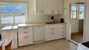 Une cuisine avec des meubles blancs, un lave-vaisselle et une fenêtre donnant sur un paysage montagneux.