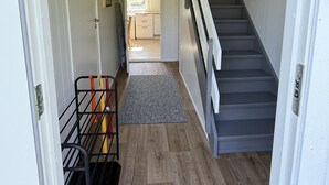 Un couloir avec un escalier, une porte, un radiateur et une fenêtre.