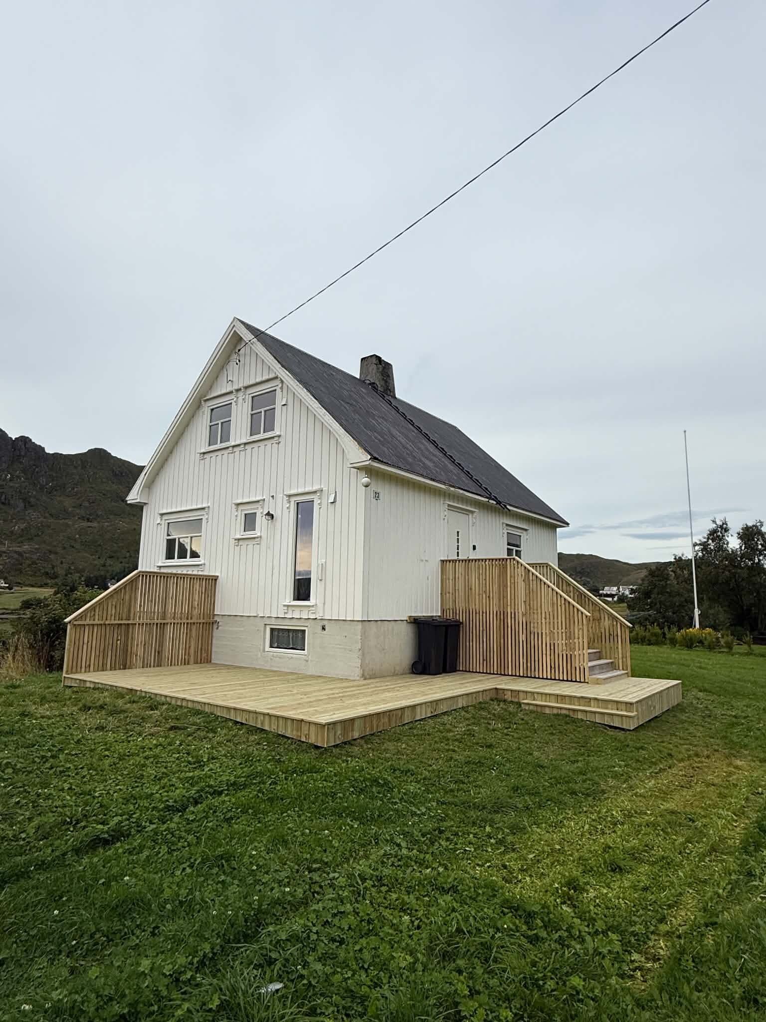 Una casa blanca de dos pisos con un porche frontal pequeño y una terraza de madera.