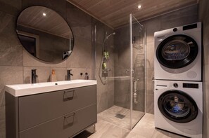 Een moderne badkamer met een grote spiegel, een wastafel, een douche en een gestapeld wasmachine en droger.