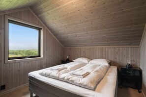 Een slaapkamer met een groot raam, houten plafond en een bed met witte lakens.