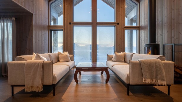 A spacious room with two sofas facing a fireplace, large windows, and a wooden floor.