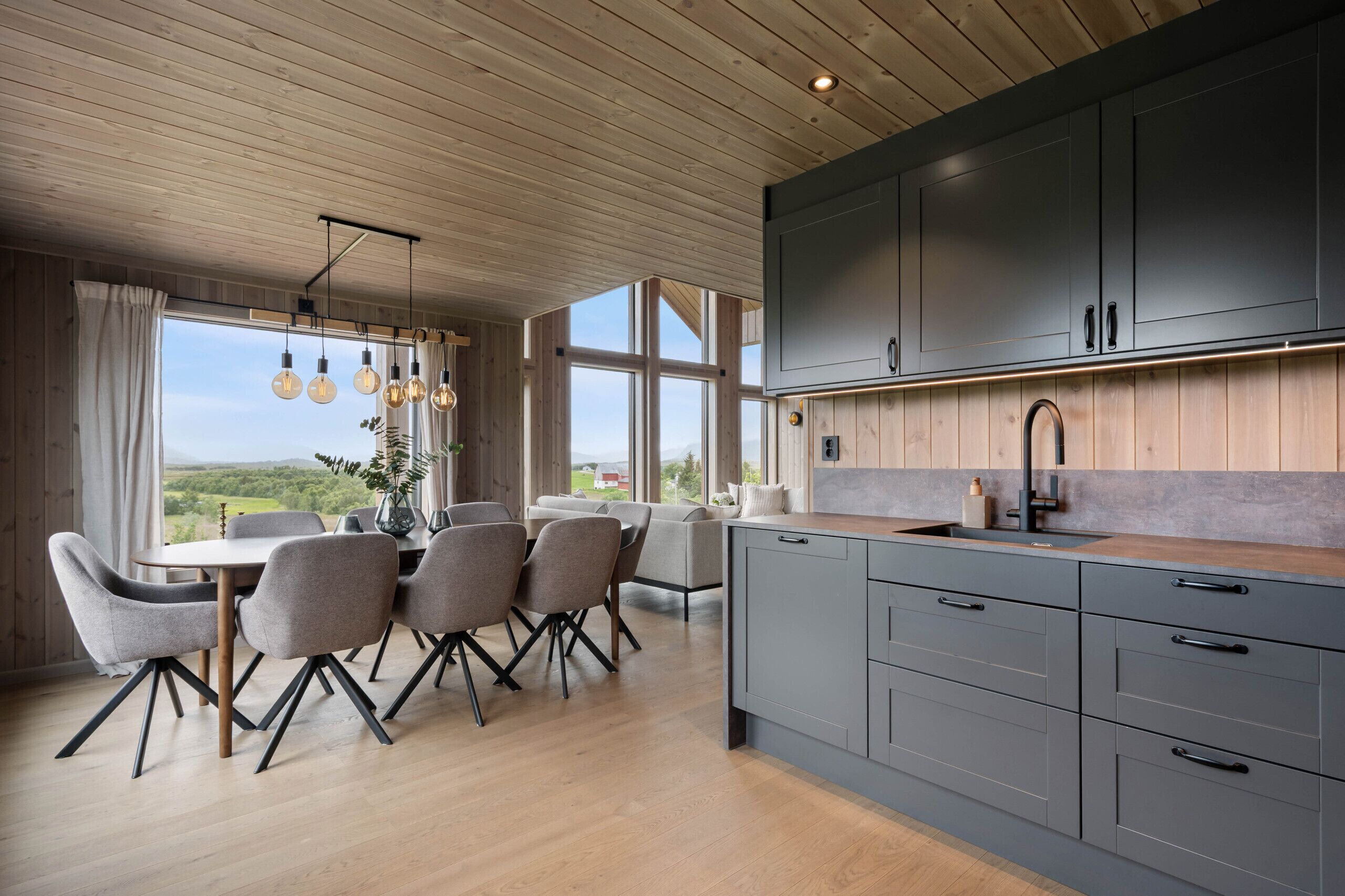 A modern kitchen with grey cabinets, a wooden ceiling, and a dining area with a table and chairs.