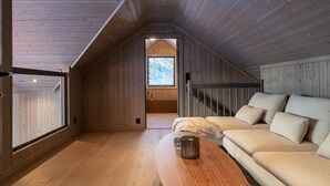 A wooden interior with a sloped ceiling, a sofa, a table, and a window.