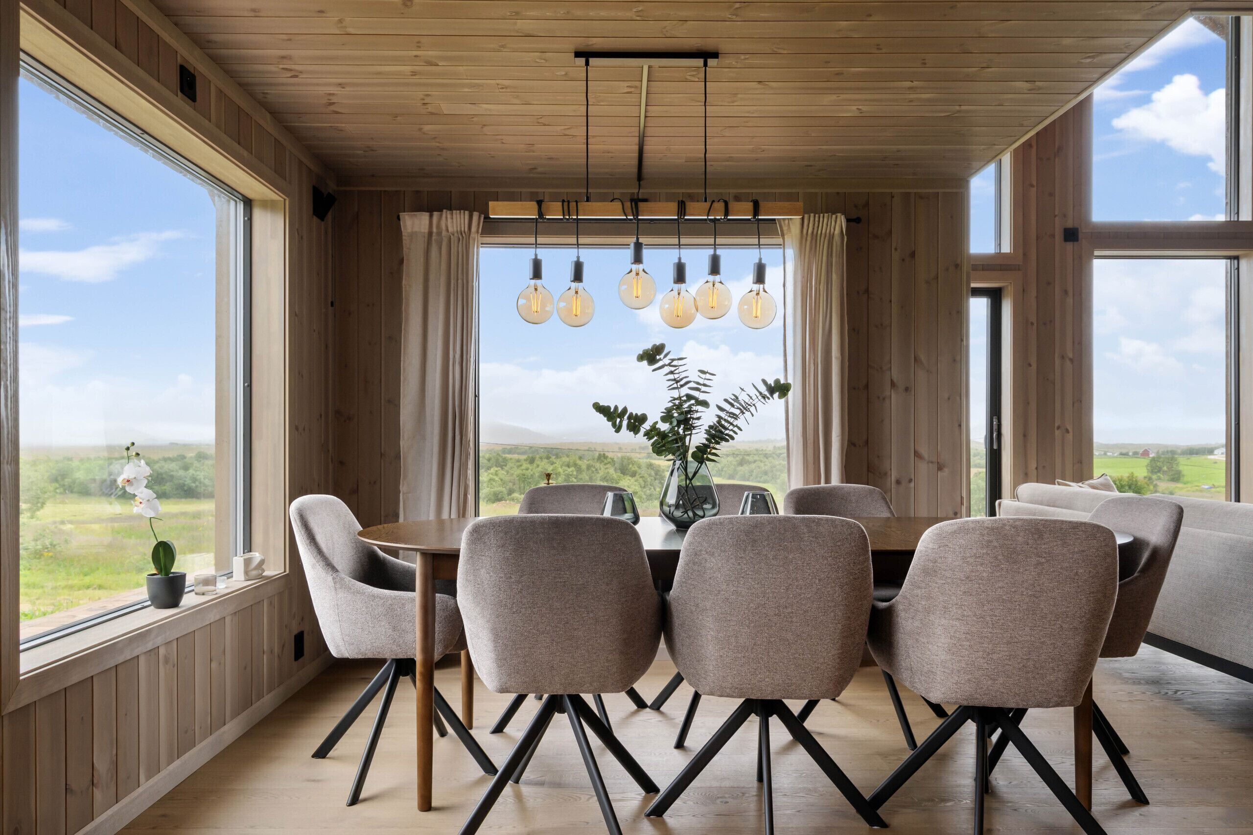 Un espace repas doté d’un plafond en bois, de grandes fenêtres et d’une table entourée de chaises.