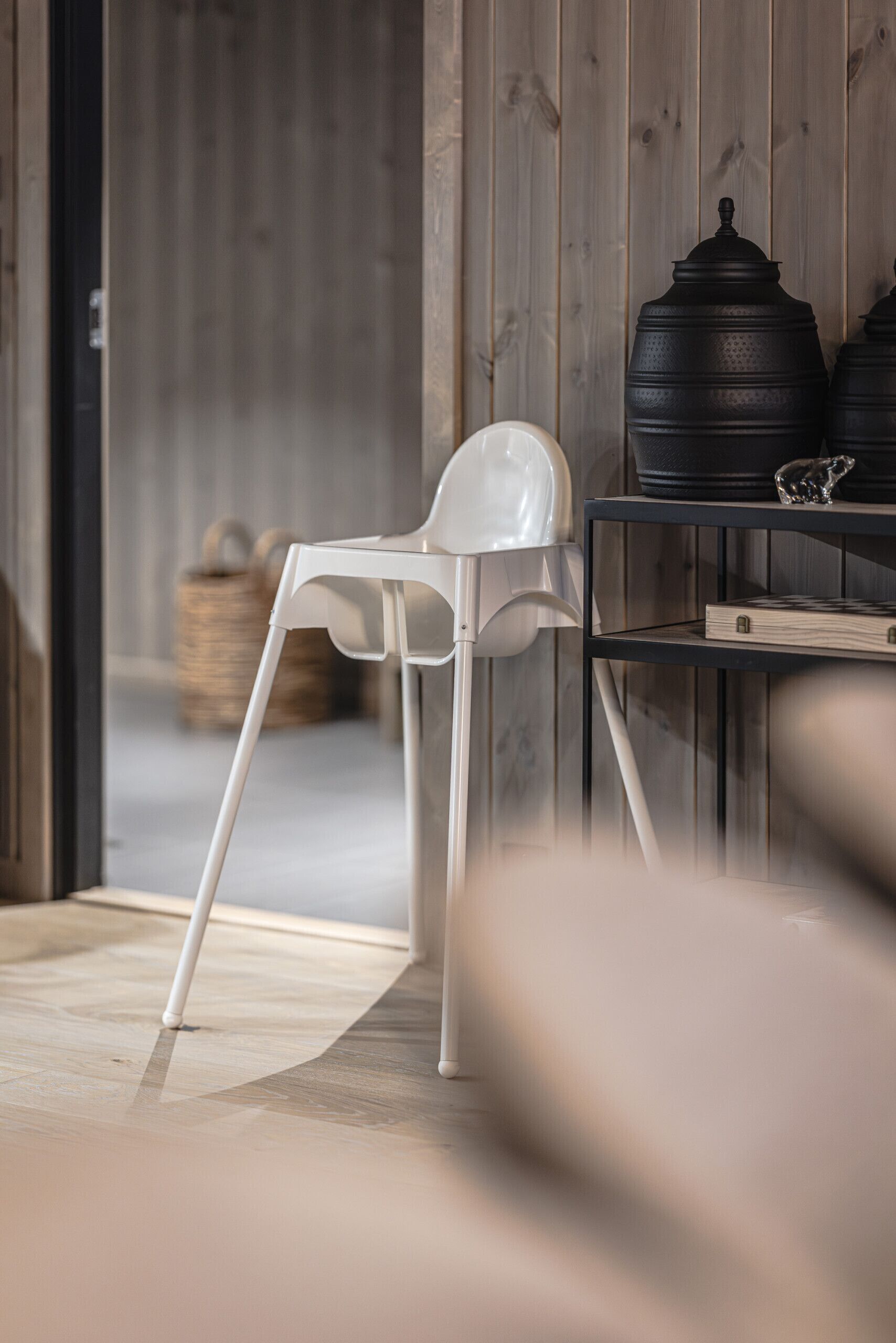A white chair, a table with black containers, and a wooden wall.