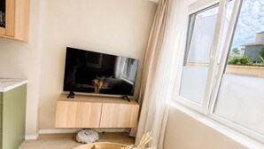 Ett modernt vardagsrum med en platt-TV, ett runt soffbord med glasskiva och ett fönster med gardiner.