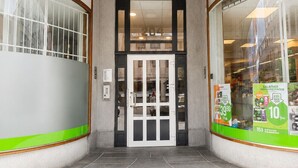 En byggnadsentré med numret ’204’ ovanför dörren, en butiksfasad av glas och ett område framför byggnaden som är belagt med tegelstenar.