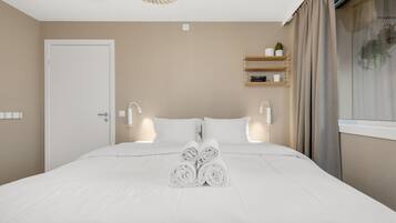 Ein Hotelzimmer mit einem ordentlich bezogenen Bett, Nachttischlampen, einem Ablagefach für Toilettenartikel und einem Fenster mit Vorhängen.