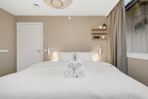 Ein Hotelzimmer mit einem ordentlich bezogenen Bett, Nachttischlampen, einem Ablagefach für Toilettenartikel und einem Fenster mit Vorhängen.