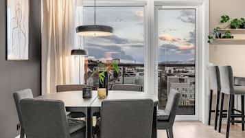 Ein Essbereich mit Tisch, Stühlen, einer Pendelleuchte, einer Pflanze und Blick auf die Stadt durch große Fenster.