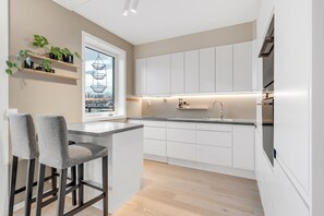 Eine moderne Küche mit weißen Schränken, einer Bar mit zwei Hockern und einem Fenster mit Blick.