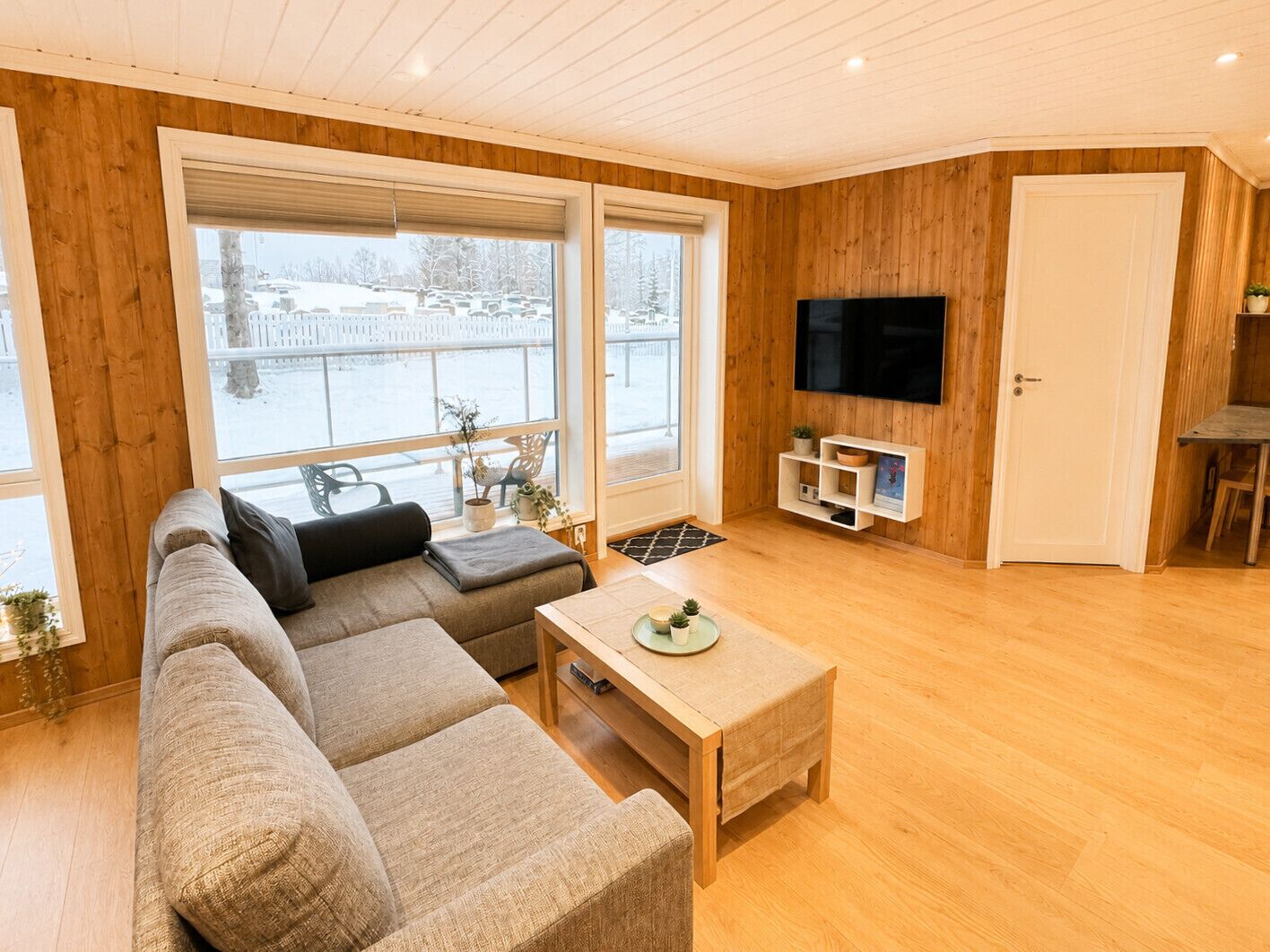 Ein modernes Wohnzimmer mit einer Eckcouch, einem Couchtisch, einem Fernseher und einer Glastür zum Balkon.