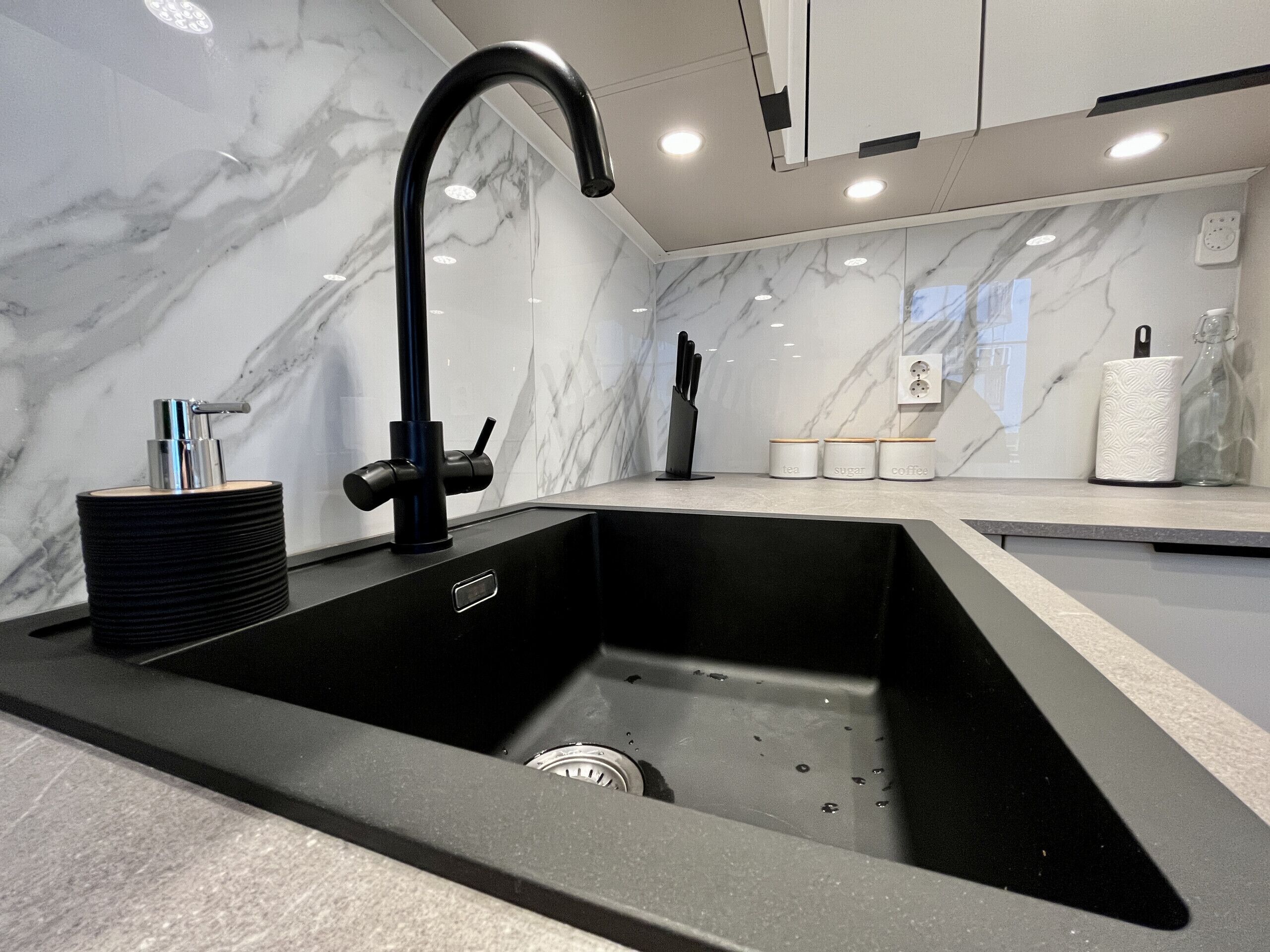 Una cocina moderna con un lavamanos negro, salpicadero de mármol y una cafetera sobre la encimera.