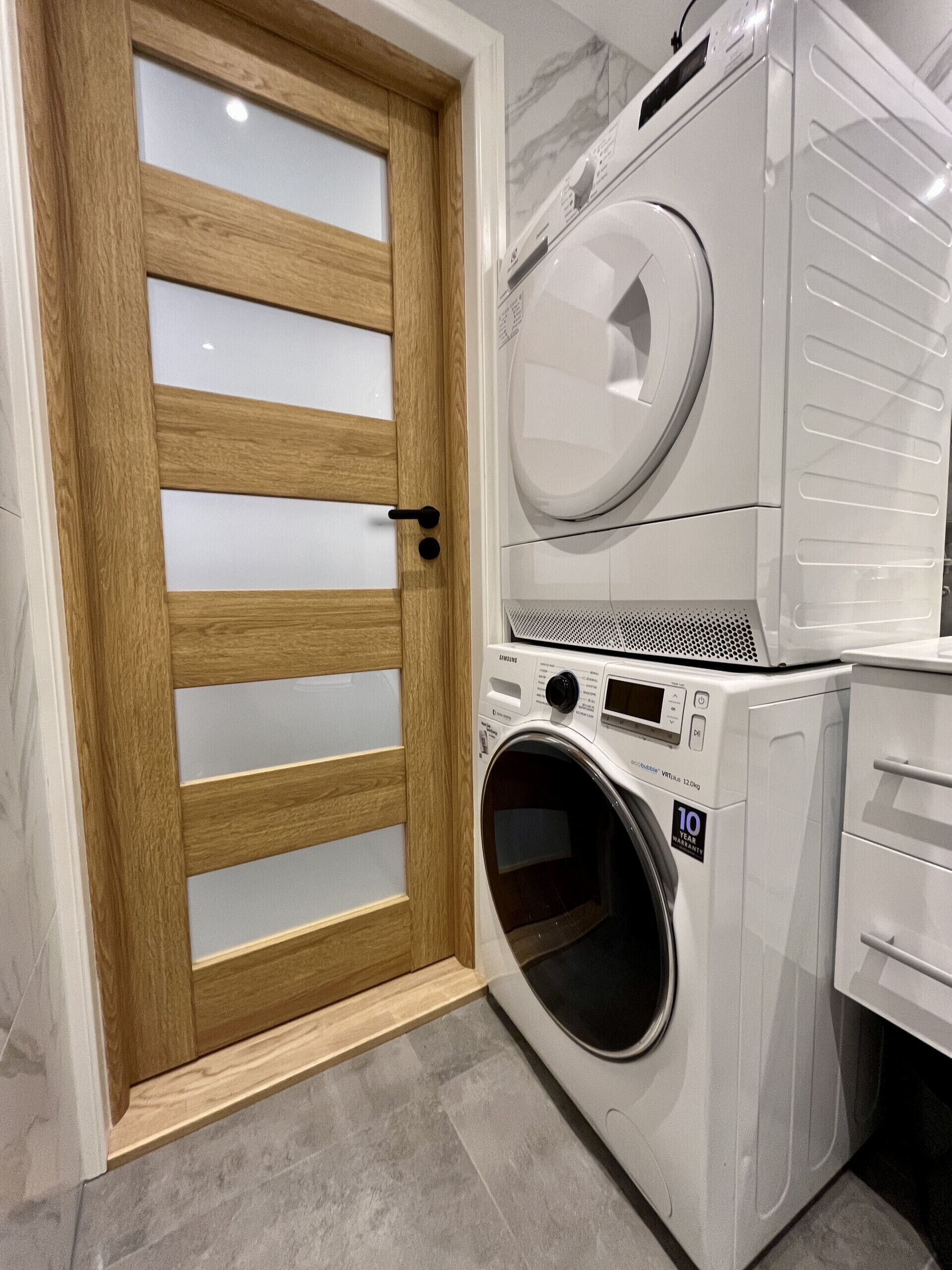 Un lavadero con puerta de madera, lavadora de carga frontal y secadora apilada.