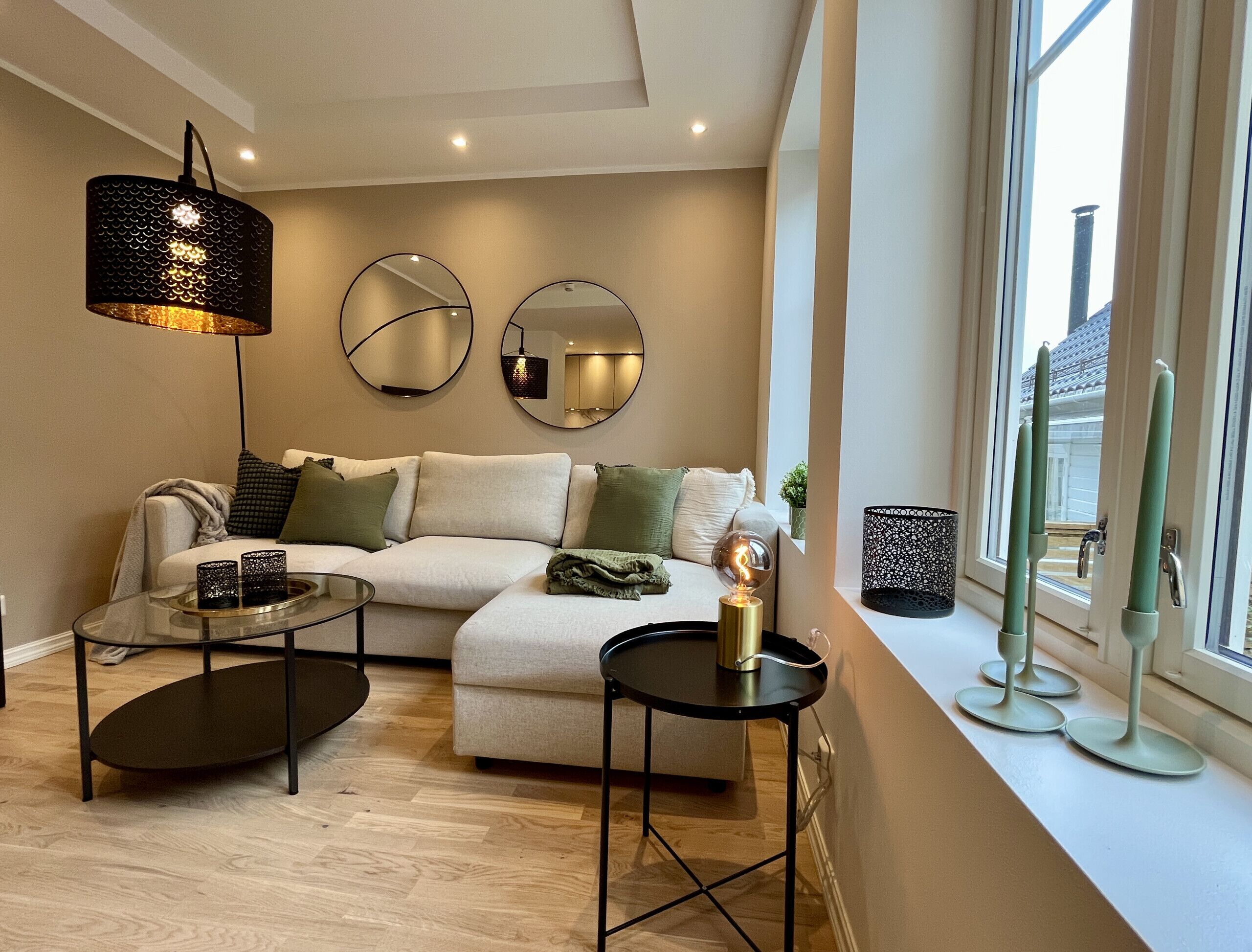 A modern living room with a sofa, two side tables, a floor lamp, and a window with candles.