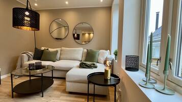 A modern living room with a sofa, two side tables, a floor lamp, and a window with candles.
