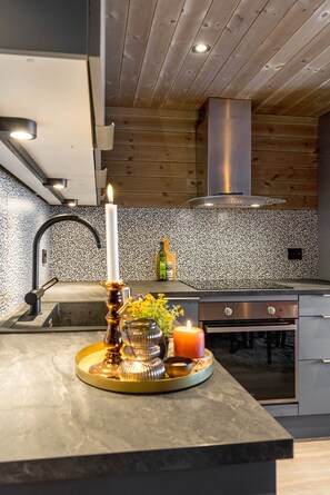 A modern kitchen with a wooden ceiling, a stainless steel range hood, and a black faucet.