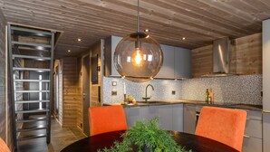 A modern kitchen with a round dining table, orange chairs, and a hanging light fixture. - Modern apartment in Golsfjellet (Gol)