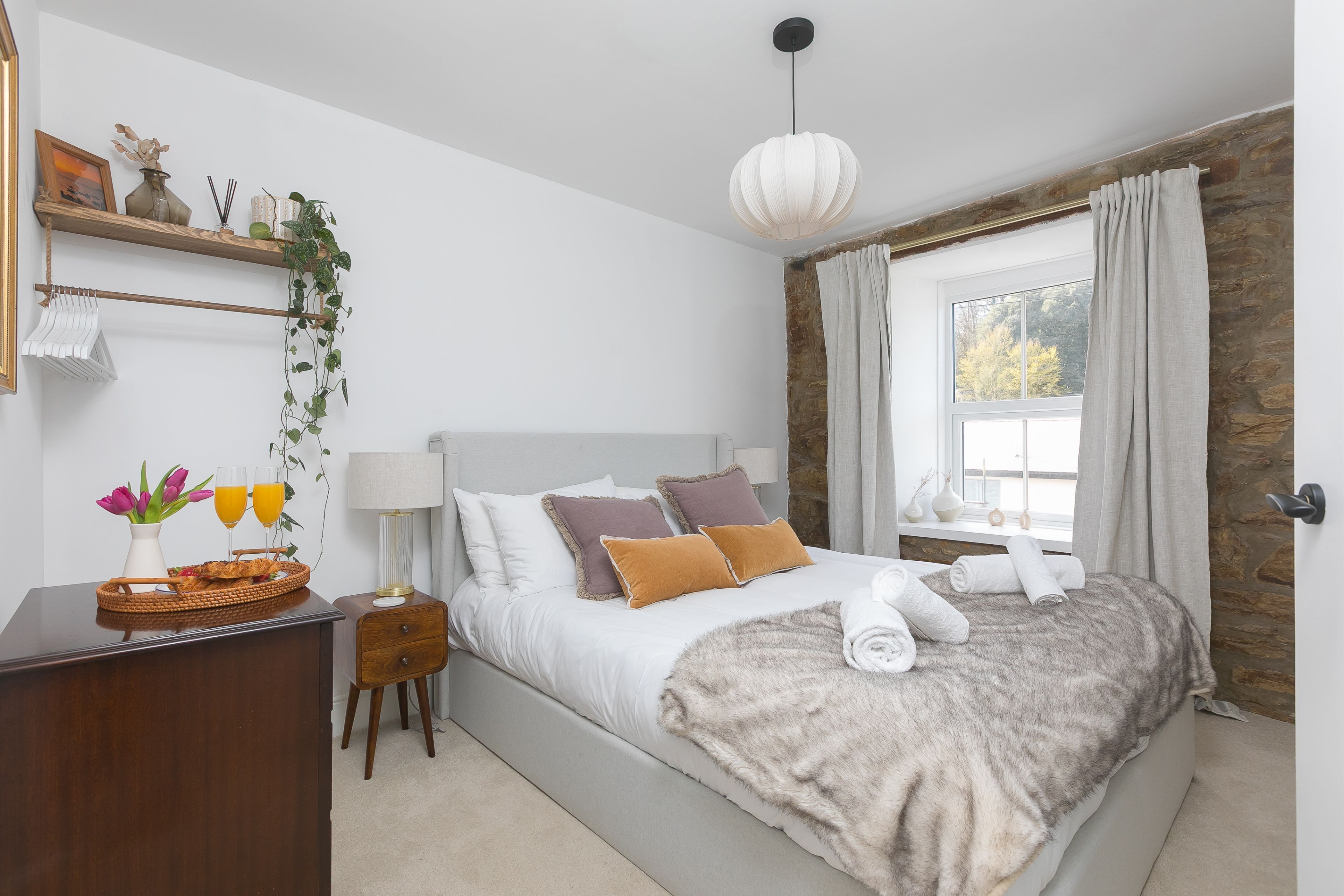 A bedroom with a bed, bedside table, lamp, and a window with curtains.