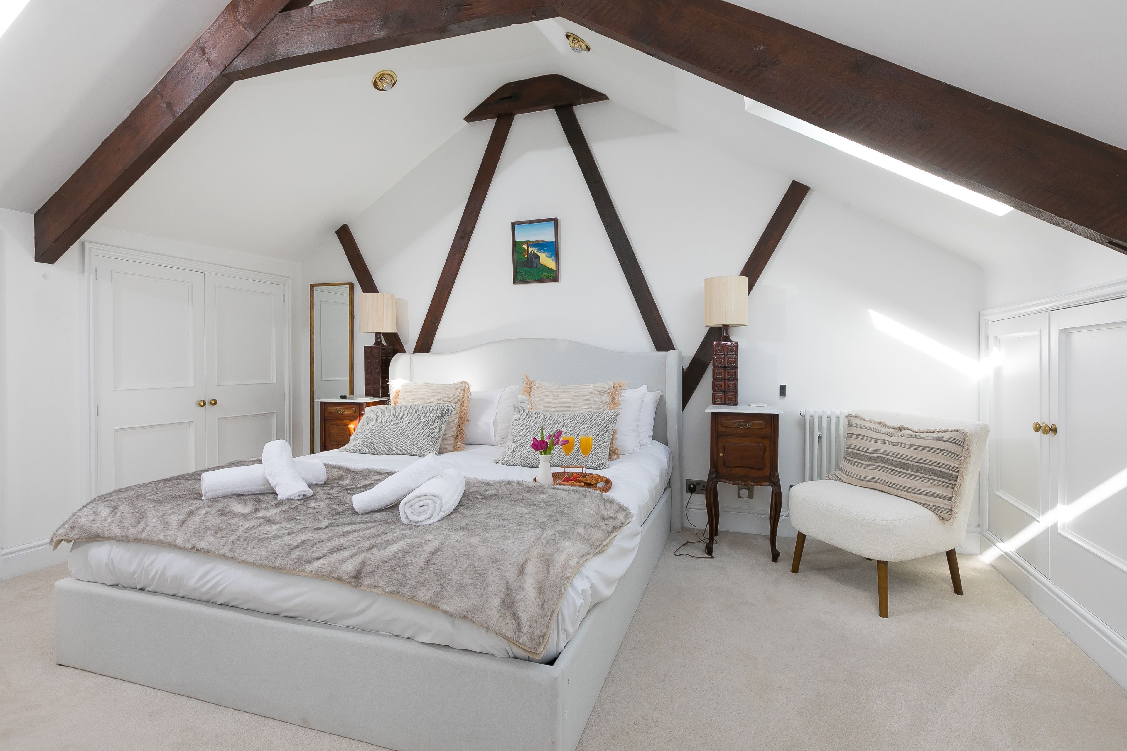 Ein Schlafzimmer mit einem großen Bett, einem Sessel, einem Nachttisch und einem Bild an der Wand.