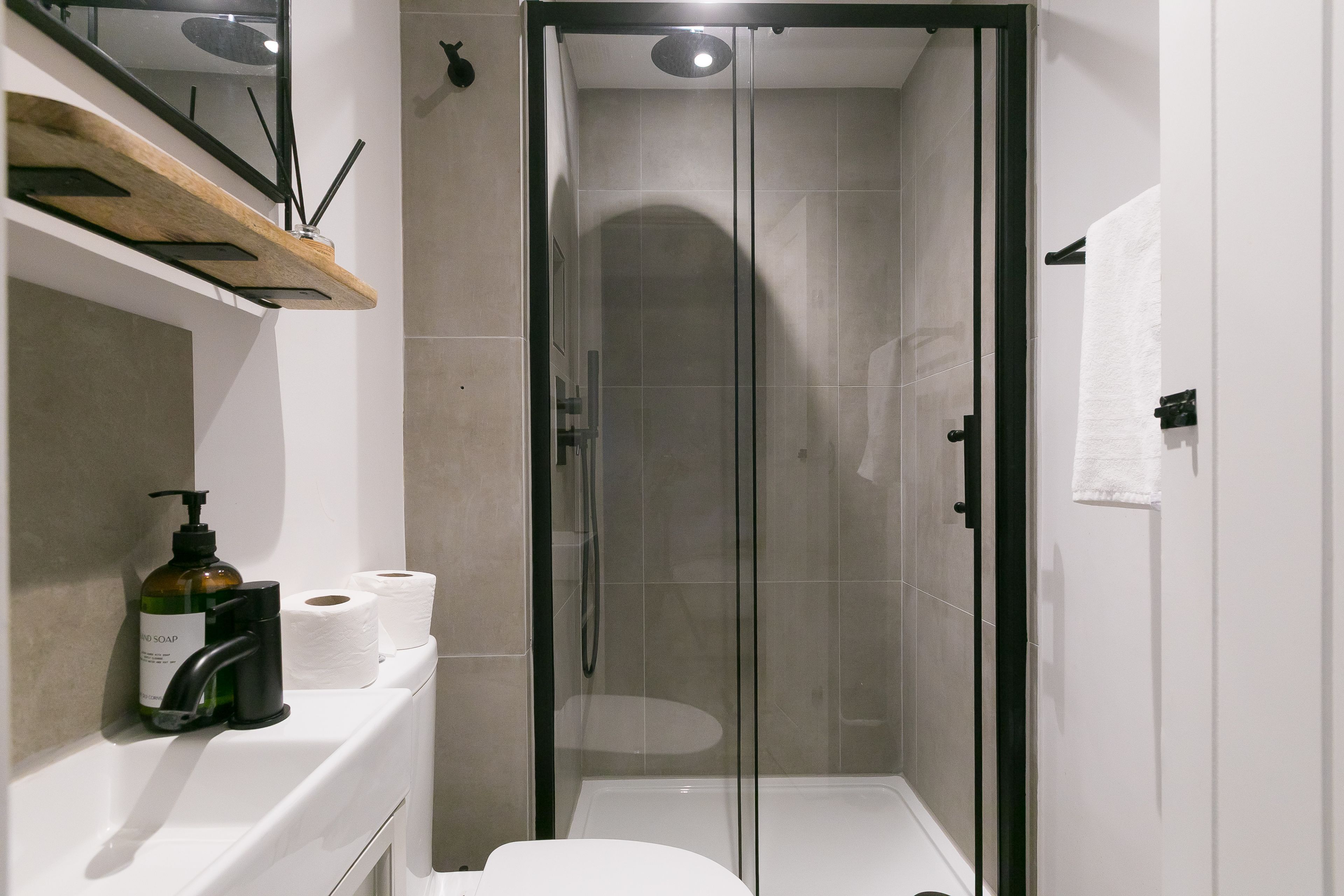Un baño moderno con ducha de vidrio, inodoro blanco y un estante con artículos de tocador.