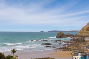 A coastal beach scene with rocky cliffs, a sandy beach, and a wooden structure with a sign. - 1 The Old Corn Store, St Agnes – Sleeps 8 – Terrace – Dog-Friendly (St Agnes)
