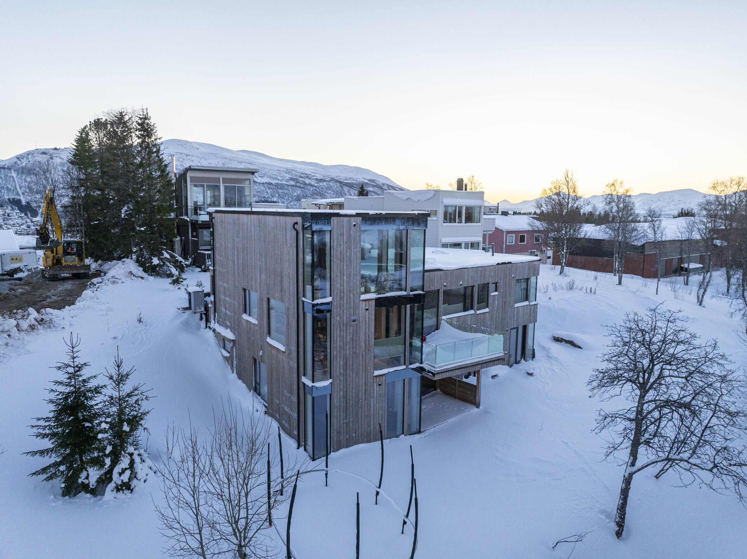 Un bâtiment moderne à plusieurs étages, doté de grandes fenêtres et d’un balcon, entouré d’un paysage enneigé et d’arbres.
