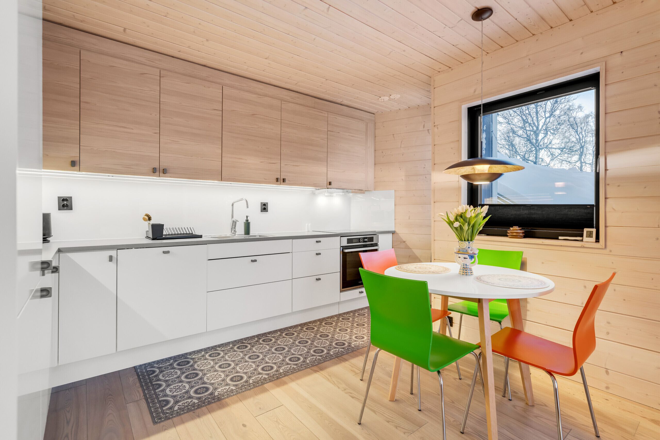 A modern kitchen with white cabinets, a round dining table, and colorful chairs.