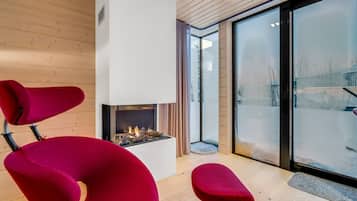 Un interior moderno con chimenea, sillas rojas y un gran ventanal que da al exterior.